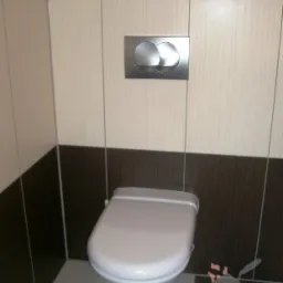 Nowoczesna toaleta podwieszana z chromowanym przyciskiem spłukującym na ścianie wyłożonej beżowo-brązowymi płytkami ceramicznymi.